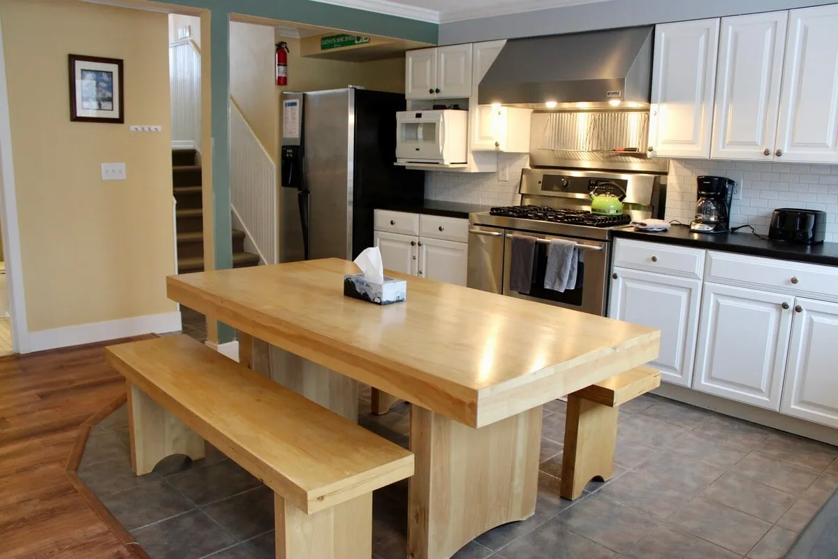 A warm dining area with a large wooden table set adjacent to kitchen appliances and white cabinetry. The table is spacious enough for group meals, games, or laughter-filled gatherings, highlighting the social heart of the home.