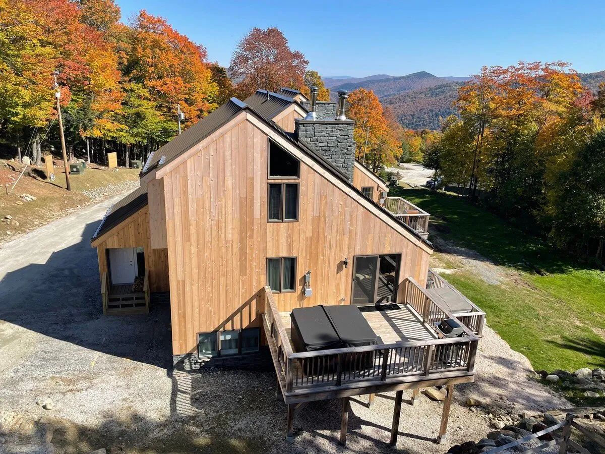 An inviting exterior deck with comfortable seating, surrounded by autumn foliage and mountain views. The wooden exterior of the house is visible, and the deck is ideal for sipping morning coffee or enjoying the sunset.