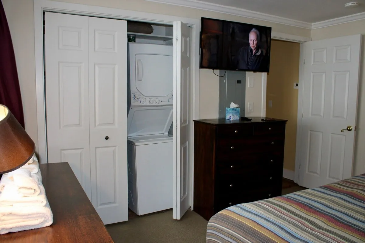 A practical laundry area with a washer-dryer unit, located within an inviting interior that also features a television, dresser, and cozy bed. The setup is both functional and welcoming, ensuring guests have everything needed to keep their gear fresh during an adventure-filled stay.