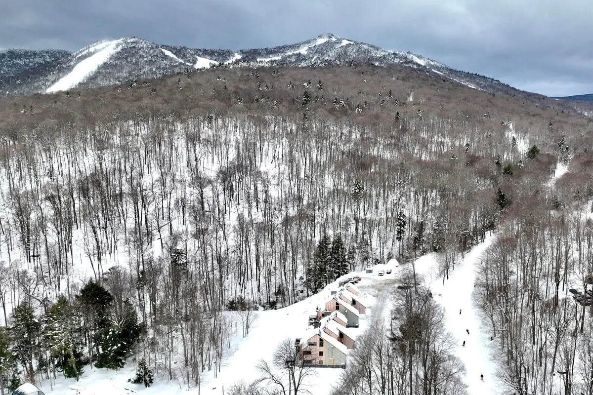 A tranquil winter scene with snow-covered mountains, scattered pine trees, and cozy cabins nestled in the foreground. The setting embodies a classic ski resort feel and showcases the natural beauty and winter sports atmosphere of Killington.