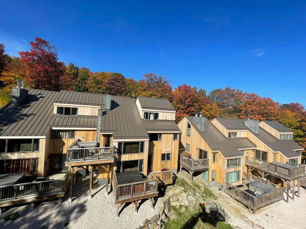 A picturesque exterior shot of Trailside Village, featuring charming wooden chalets with balconies framed by vibrant autumn foliage. The inviting balconies and cozy outdoor ambiance hint at the mountain setting and opportunities for enjoying stunning sunset views together.