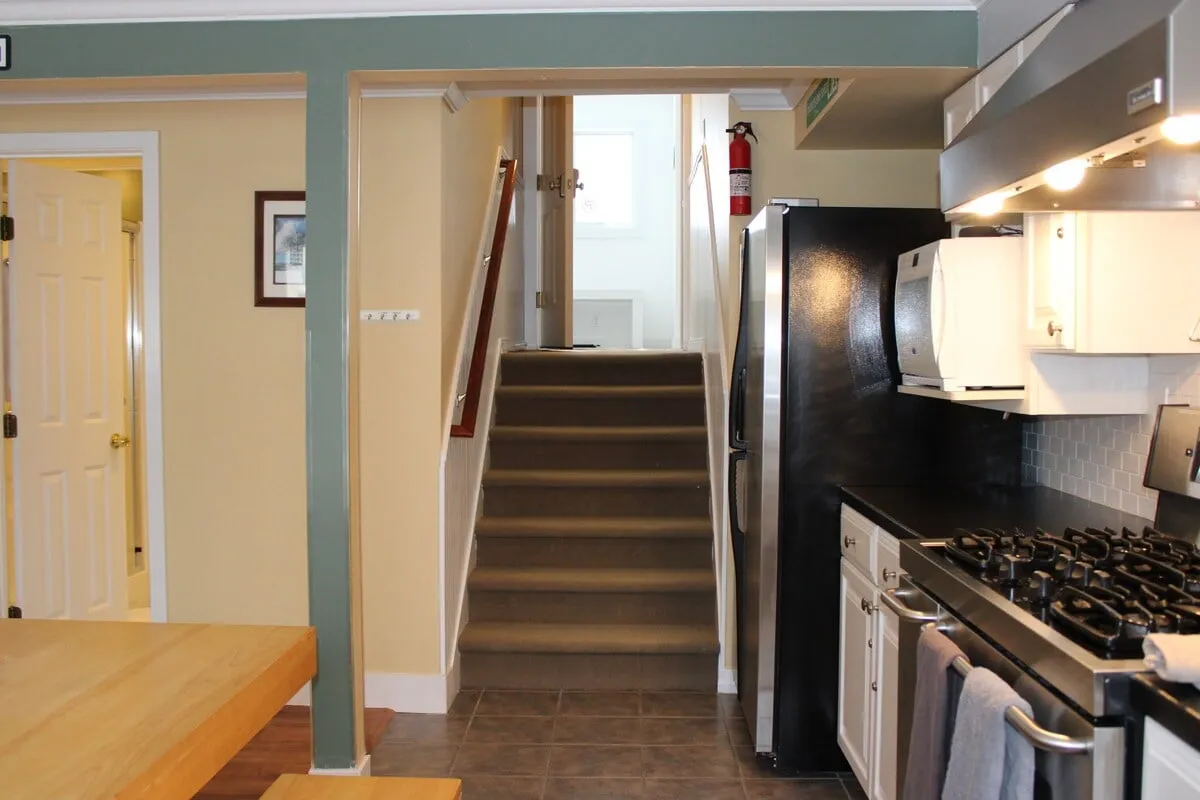 This image captures a welcoming interior space featuring a staircase, kitchen appliances, and a dining table, suggesting easy transition from indoor activities like cooking and dining to outdoor adventures. The open plan and visible entry points hint at accessibility to the outside world, echoing the theme of coming together after a day of exploring Killington's summer and fall activities.