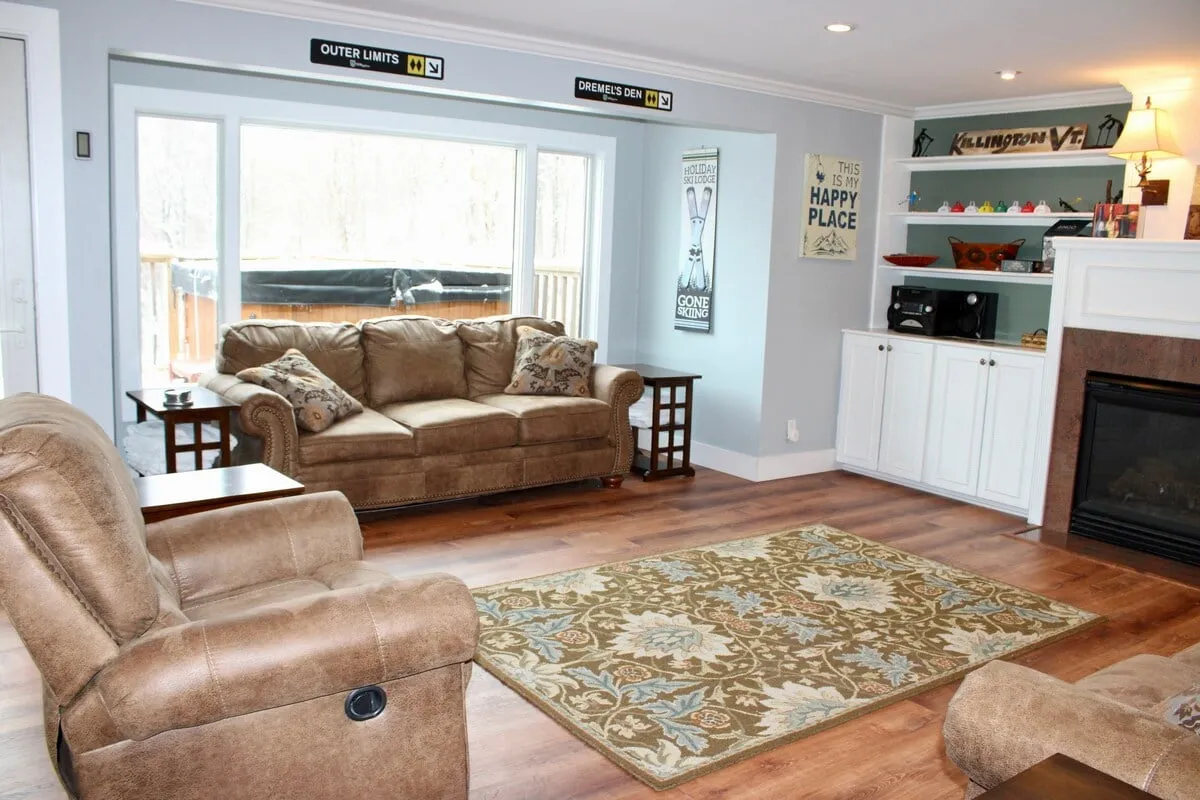 A welcoming living room featuring a comfortable sofa arranged around a glowing fireplace. Large windows offer sweeping mountain views, and a decorative rug anchors the space. The atmosphere is relaxed, inviting guests to unwind with a cup of coffee or gather for a movie night by the fire.