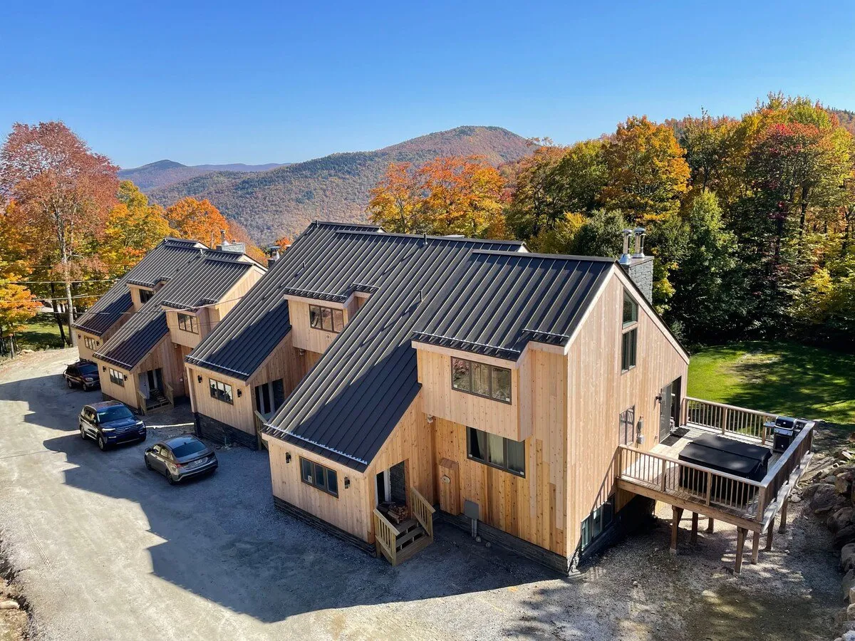 A rustic wooden house with a mountain backdrop, surrounded by nature and featuring a deck with a hot tub. While the setting is autumnal, the visible hot tub directly ties into the après-ski relaxation amenities described in the section.