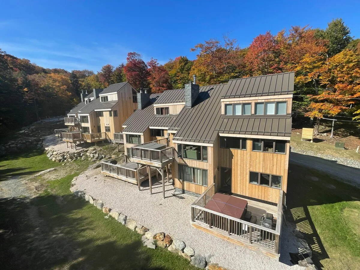 Modern wooden cabins with metal roofs nestled among colorful autumn foliage, featuring spacious outdoor decks that invite relaxation, gatherings, and barbecuing. The image evokes tranquility and the appeal of enjoying Vermont’s natural beauty from the comfort of a private retreat.