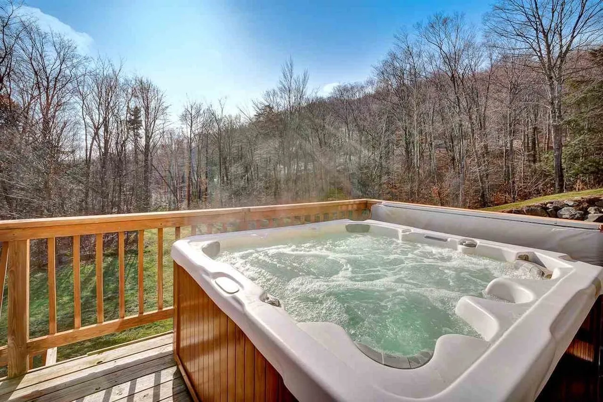 An exterior scene showing the hot tub on a wooden deck overlooking a natural landscape, with tranquil surroundings ideal for relaxation. The open-air setting conjures images of stargazing or unwinding in the fresh mountain air.